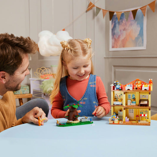 young girls playing with LEGO house with her father present, both are smiling