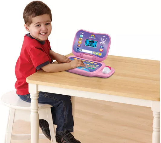 toddler sitting at table with pink and purple toy laptop
