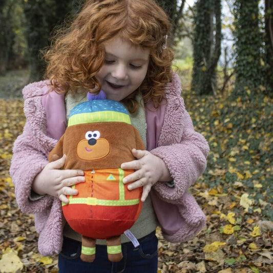Child holding a colorful plush toy in an outdoor setting with fallen leaves.