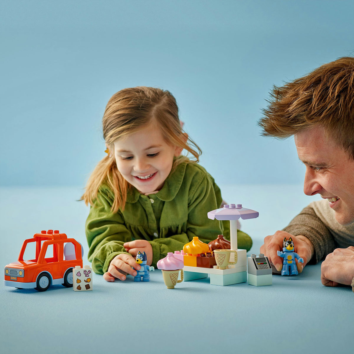 Girl and father playing with bluey lego icecream toys on blue background 