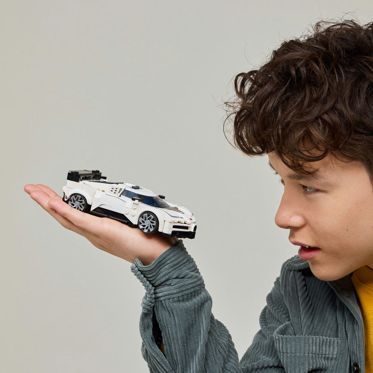 Young boy holding white LEGO car in the palm of his hand 