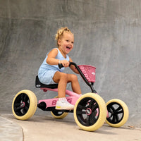 A young child riding a pink and black tricycle with yellow wheels in front of a concrete wall.