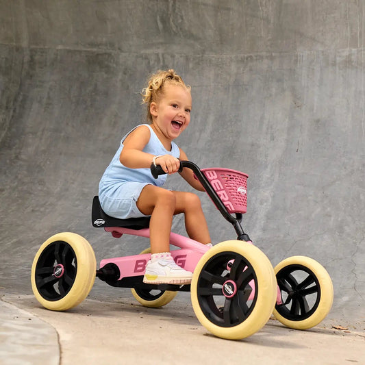 A young child riding a pink and black tricycle with yellow wheels in front of a concrete wall.