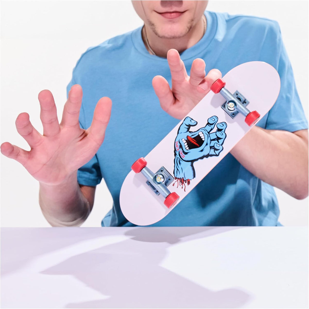 Person holding a small skateboard with a graphic design on a white background