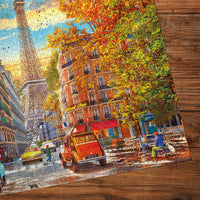 The Gibsons - Autumn in Paris 1000 Piece Jigsaw Puzzle features a picturesque Parisian street, classic cars, and a cozy atmosphere.
