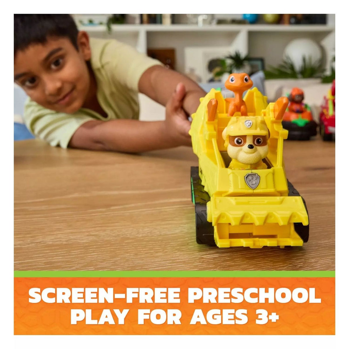 A young boy playing with the yellow construction vehicle on a table. the vehicle has a small dog and dinosaur figurine 