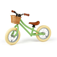 Green balance bike with brown basket, seat and handles on white background