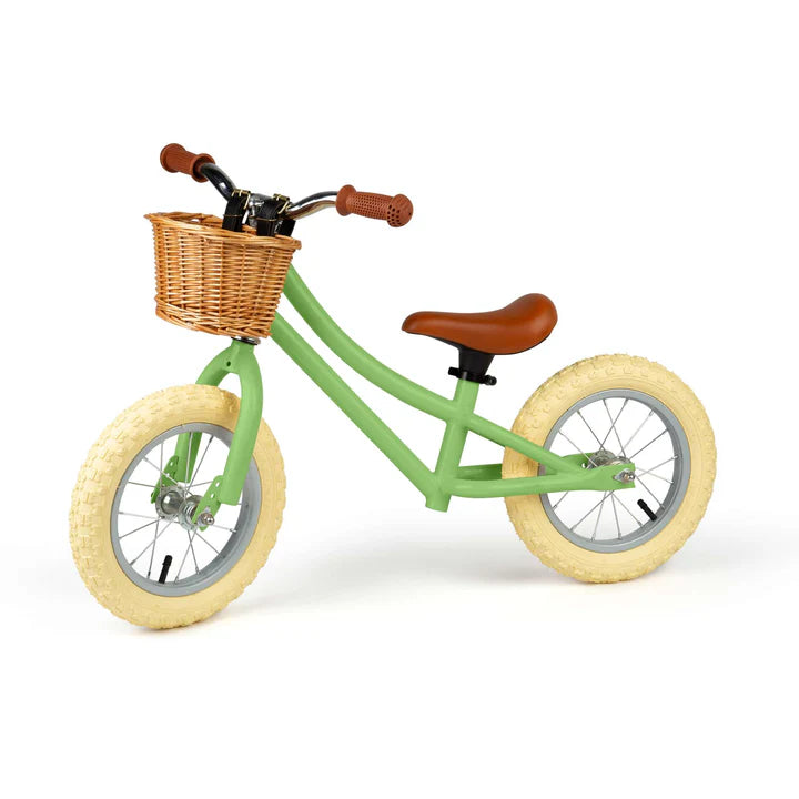 Green balance bike with brown basket, seat and handles on white background