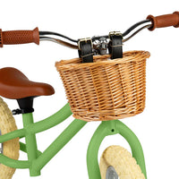 close up of Green balance bike with brown basket, seat and handles on white background