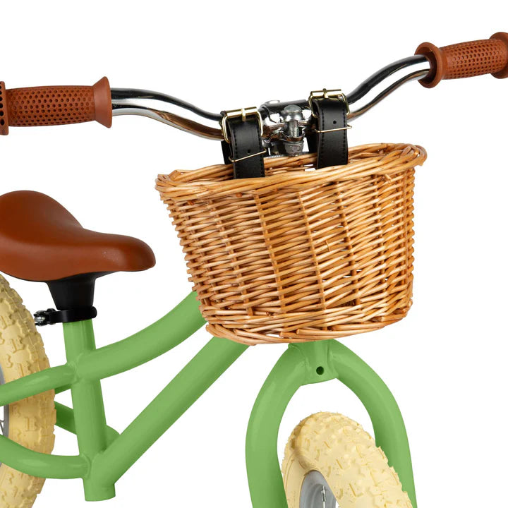 close up of Green balance bike with brown basket, seat and handles on white background