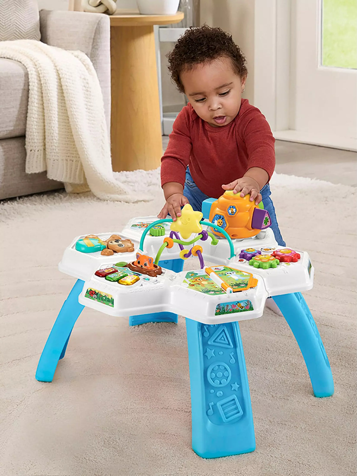 baby playing with brightly coloured activity table in living room 