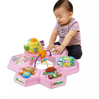 baby playing with top of pink activity table on white background 