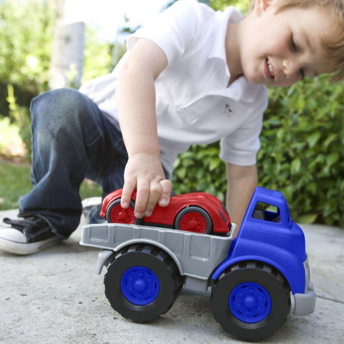 boy playing with flatbed truck toy and racecar 