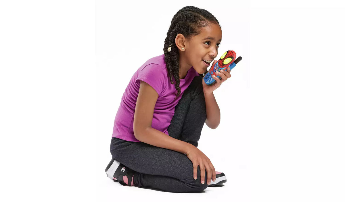 young girl holding a blue spider man walkie talk and smiling on a white background
