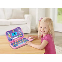 toddler sitting at table with pink and purple toy laptop