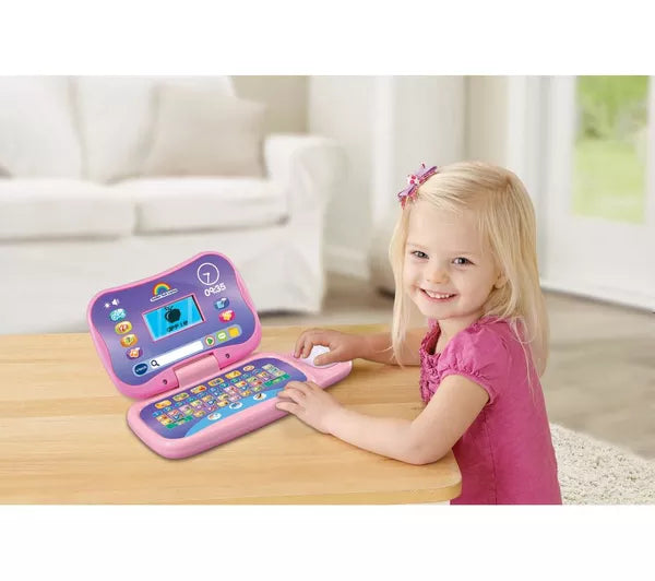 toddler sitting at table with pink and purple toy laptop