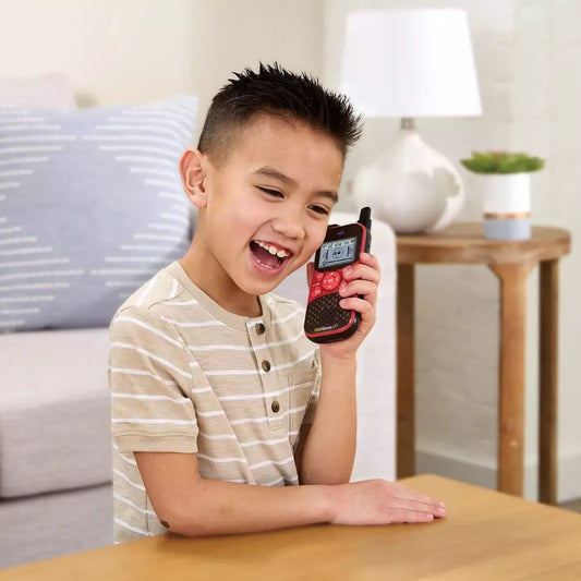 young boy smiling holding a red walkie talkie up to his ear 