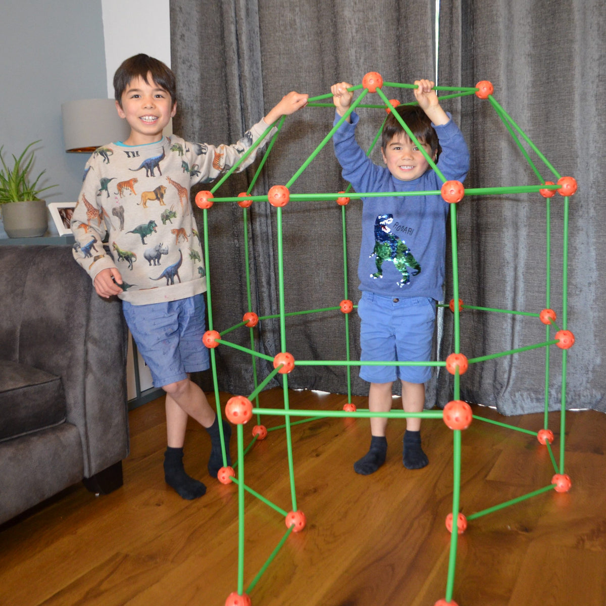 Two children playing with a green and orange geometric structure indoors.