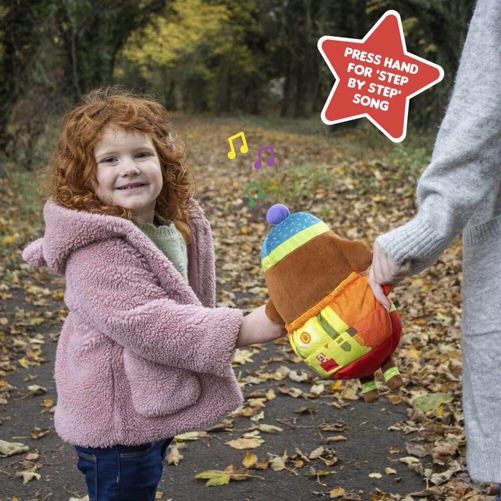 Child holding a colorful plush toy outdoors with a star-shaped sign indicating a song can be pressed.