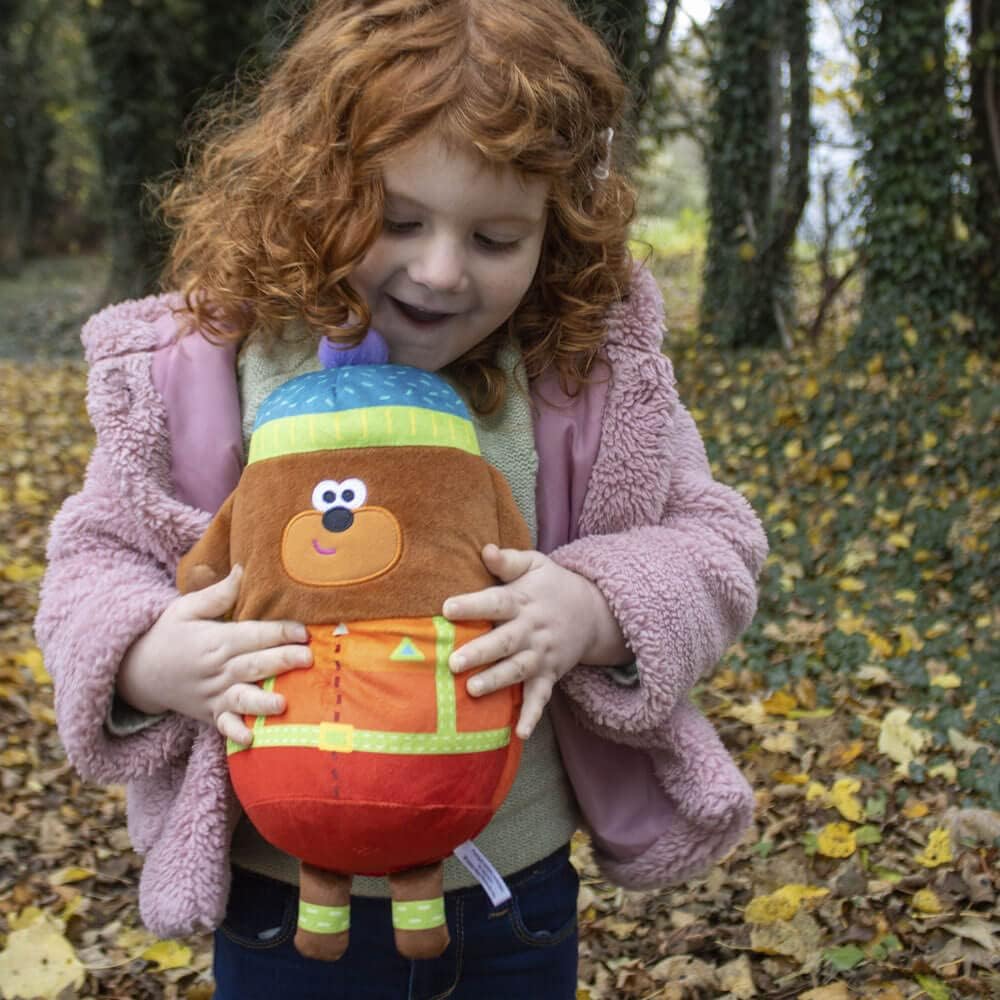 Child holding a colorful plush toy in an outdoor setting with fallen leaves.